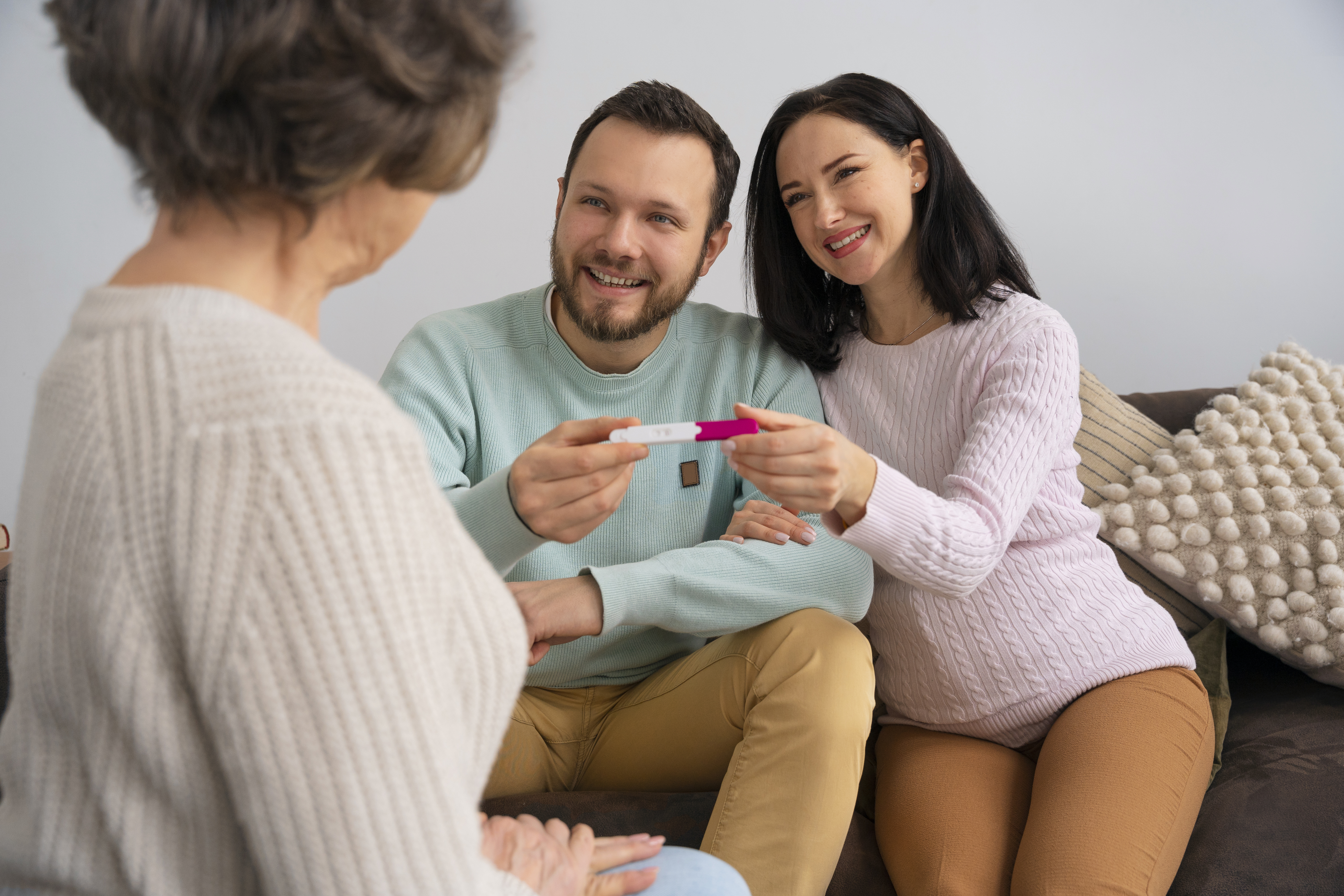 A smiling young couple sitting on a sofa and holding up a modern, digital contraception device or fertility monitor to show a healthcare provider, signifying an informed choice about reproductive health. This emphasizes effective options provided by a reputable family planning clinic